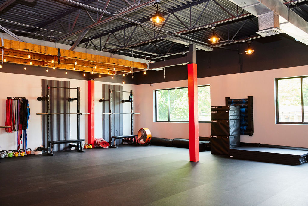 Interior of the Strong on Center studio with squat racks, plyo boxes, kettlebells, and string lights along the wood beams.