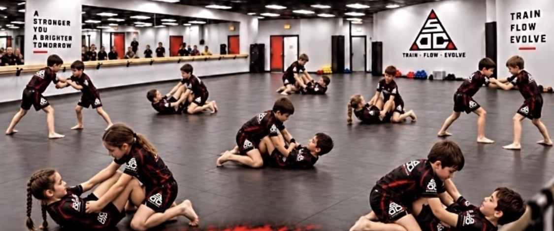 Kids practicing no-gi jiu-jitsu drills in pairs across the studio mat floor.