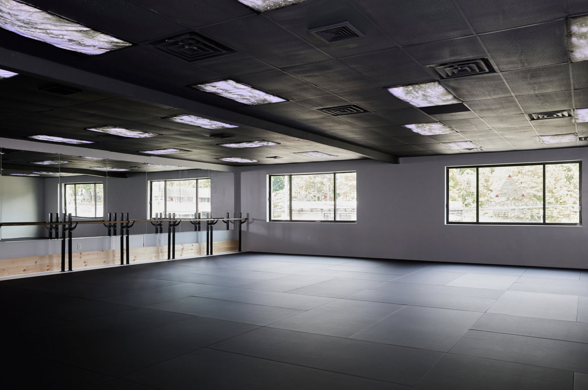 The barre and mat studio at Strong on Center with mirrored wall, ballet barre, and black training mats.